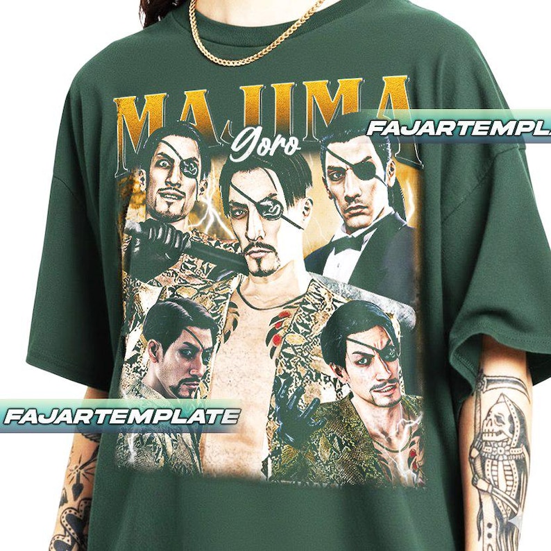 May include: Dark green t-shirt featuring a graphic of a man with an eyepatch, with the text "MAJIMA Goro" in gold lettering. The design includes multiple images of the same character in various poses. The shirt has a crew neck and short sleeves.
