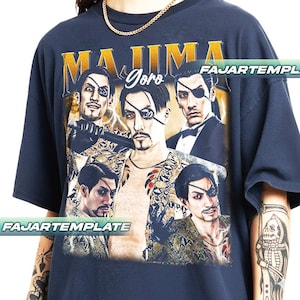 May include: Navy blue graphic t-shirt featuring a collage of a character with an eyepatch, the text "MAJIMA Goro" in gold lettering, and lightning bolt accents. The shirt has a crew neck and short sleeves.