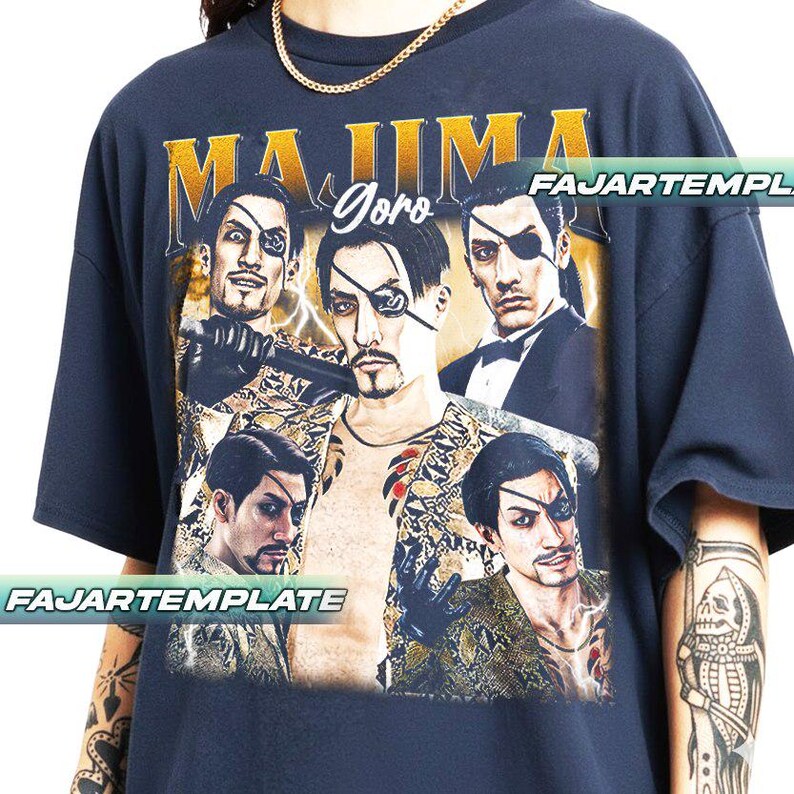 May include: Navy blue graphic t-shirt featuring a collage of a character with an eyepatch, the text "MAJIMA Goro" in gold lettering, and lightning bolt accents. The shirt has a crew neck and short sleeves.
