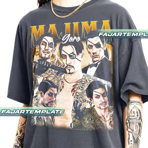 May include: Dark gray t-shirt featuring a graphic of a man with an eyepatch, with the text "MAJIMA Goro" in gold lettering. The design includes multiple images of the character. The shirt has a vintage, distressed look.