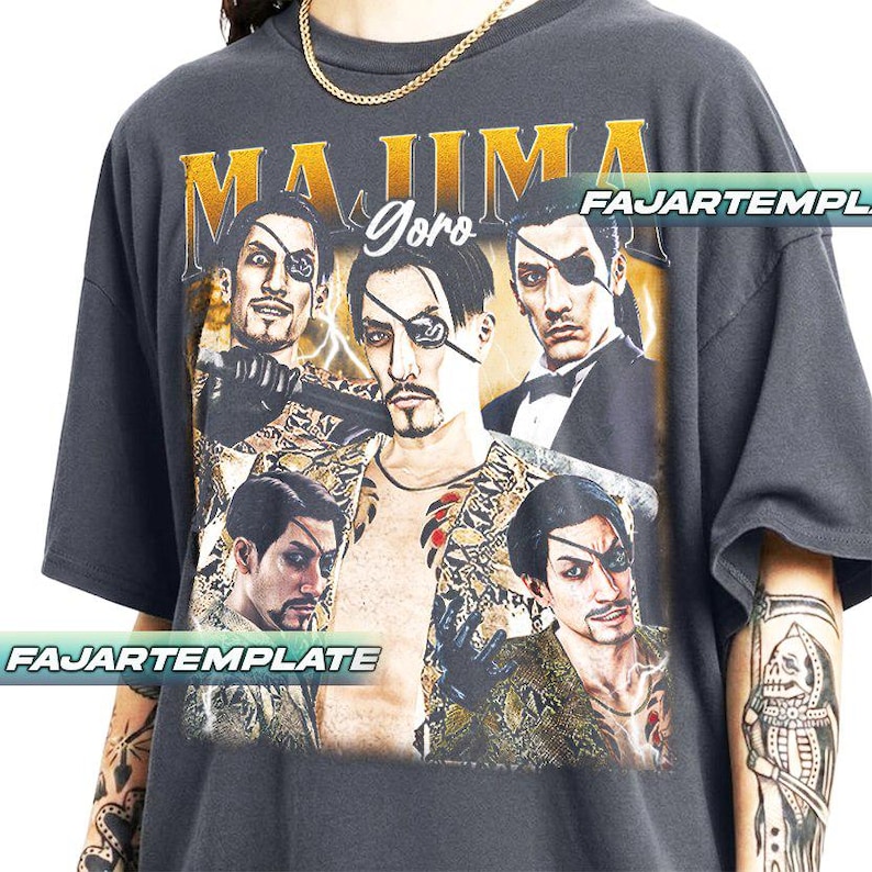 May include: Dark gray t-shirt featuring a graphic of a man with an eyepatch, with the text "MAJIMA Goro" in gold lettering. The design includes multiple images of the character. The shirt has a vintage, distressed look.