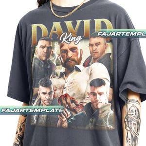 Può includere: T-shirt grigio scuro con una grafica di un uomo con la barba e più immagini dello stesso uomo. La parola "DAVID" è stampata sopra l'immagine in lettere dorate, con la parola "King" in bianco. Il testo "FAJARTEMPLATE" è stampato sulla maglietta.