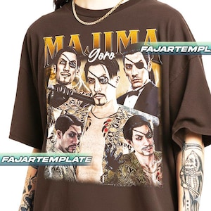 May include: Brown t-shirt featuring a graphic of a character with an eyepatch, with the text "MAJIMA Goro" in gold. The design includes multiple images of the character. The shirt has short sleeves and a relaxed fit.