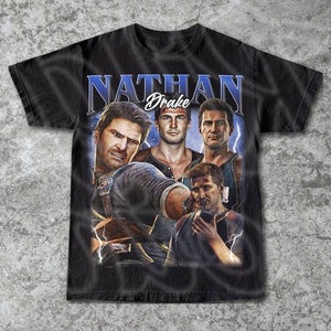 May include: Black t-shirt featuring a graphic of Nathan Drake from the Uncharted video game series. The design includes multiple images of the character with the name "Nathan Drake" in a blue and white font.