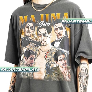 May include: Dark gray t-shirt featuring a graphic of a man with an eyepatch, with the text "MAJIMA Goro" in gold lettering. The design includes multiple images of the character. The shirt has a vintage, worn look.