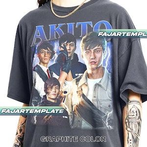 Può includere: T-shirt color grafite con una grafica di un gruppo di persone e la parola "AKITO" in blu. La maglietta presenta anche le scritte "FAJARTEMPLE" e "GRAPHITE COLOR".
