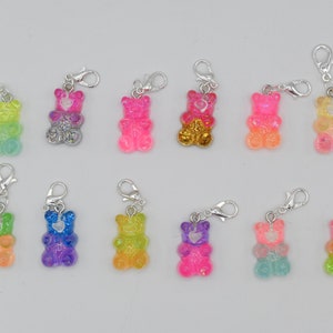 Könnte beinhalten: Zwölf Gummibärchen-Anhänger mit silbernen Karabinerhaken. Die Gummibärchen sind in verschiedenen Farben, darunter rosa, grün, blau, gelb und orange. Jedes Gummibärchen hat ein kleines Herz auf der Brust.