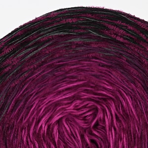 Könnte beinhalten: Eine Garnrolle mit einem Farbverlauf von Dunkelviolett bis Schwarz. Das Garn ist zu einem Kreis gewickelt und hat eine flauschige Textur.