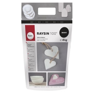 Könnte beinhalten: Eine Packung weißes Gießpulver, beschriftet mit "RAYSIN 100* BASIC", mit einem Gewicht von 4 kg. Das Bild zeigt weiße herzförmige Ornamente und andere Bastelartikel. Die Packung zeigt auch die Marke "Rayher."