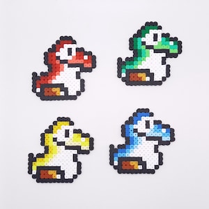 Op de afbeelding: Vier pixel art figuren van een dinosaurusachtig wezen in rood, groen, geel en blauw. Elke figuur heeft een witte buik, bruine accenten en zwarte contouren. De figuren zijn gerangschikt op een witte achtergrond.
