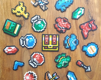 Könnte beinhalten: Eine Sammlung bunter Pixel-Art-Designs, darunter eine Truhe, ein Schlüssel, ein Trank, eine Bombe, ein Herz, ein Pilz, eine Blume, ein Stern, ein Schwert, ein Schild und eine Krone. Die Designs sind aus kleinen Plastikperlen gefertigt.