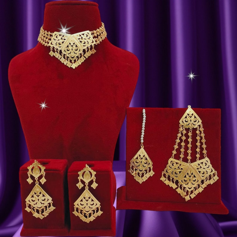 May include: A gold-tone jewelry set with a delicate choker necklace, matching earrings, and a traditional Indian nose ring. The jewelry features intricate floral designs and dangling accents.
