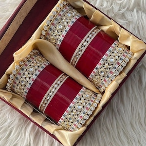 May include: Two ornate red bangles with gold and white embellishments, set in a red velvet box with gold lining.
