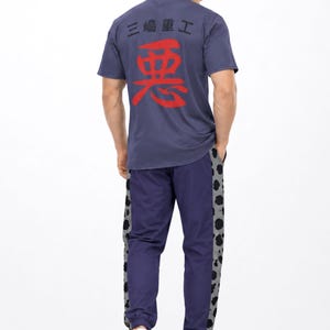 Pode incluir: Uma t-shirt azul de manga curta com um grande caractere japonês vermelho e texto japonês preto mais pequeno nas costas, combinada com calças de fato de treino azuis com painéis laterais com padrão de leopardo cinzento e preto e sapatilhas brancas.