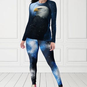 Puede incluir: Conjunto de camiseta de manga larga y leggings con un dise&ntilde;o de &aacute;guila calva. La camiseta tiene un fondo azul oscuro con un efecto de cielo estrellado y la cabeza del &aacute;guila. Los leggings tienen un patr&oacute;n de galaxia azul y blanco a juego. El texto "MAX(XX)ART" es visible.