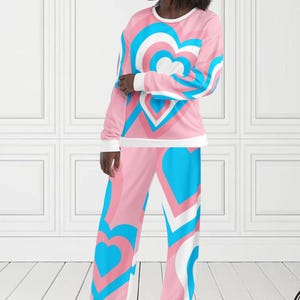 Peut inclure: Ensemble de pyjama rose avec un motif de cœur bleu, blanc et rose. Le haut à manches longues et le pantalon présentent un motif de cœur répétitif. Le haut a des poignets blancs et un col blanc. Le texte "MAX(XX)ART" est visible en haut à gauche.