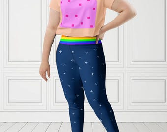 May include: A peach crop top with a pink square pattern and navy blue leggings with a white star design. The leggings have a rainbow waistband. The top is paired with navy blue leggings.