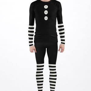 May include: A long-sleeve black shirt featuring three white circular button graphics on the chest and black and white horizontal striped sleeves, paired with black leggings that have black and white horizontal striped lower legs and black shoes.