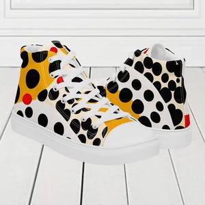 May include: High-top canvas trainers with a striking polka dot design. The pattern includes large black dots on a white and yellow backdrop, with red highlights. The trainers have white laces and a white rubber sole. The text "MAX(XX)ART" is visible.