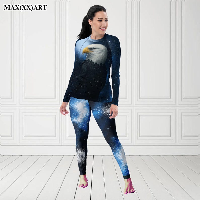 Puede incluir: Conjunto de camiseta de manga larga y leggings con un dise&ntilde;o de &aacute;guila calva. La camiseta tiene un fondo azul oscuro con un efecto de cielo estrellado y la cabeza del &aacute;guila. Los leggings tienen un patr&oacute;n de galaxia azul y blanco a juego. El texto "MAX(XX)ART" es visible.