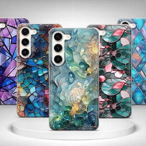 May include: Five phone cases with abstract mosaic patterns in various colours. The cases display shades of purple, blue, green, and pink. Each case has a camera aperture and a smooth, glossy surface.