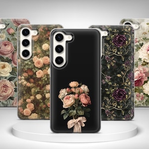 May include: A collection of phone cases with floral designs. The cases feature various patterns, including roses and other flowers in shades of pink, peach, and purple, set against black and patterned backgrounds. The cases are displayed on a white circular platform.
