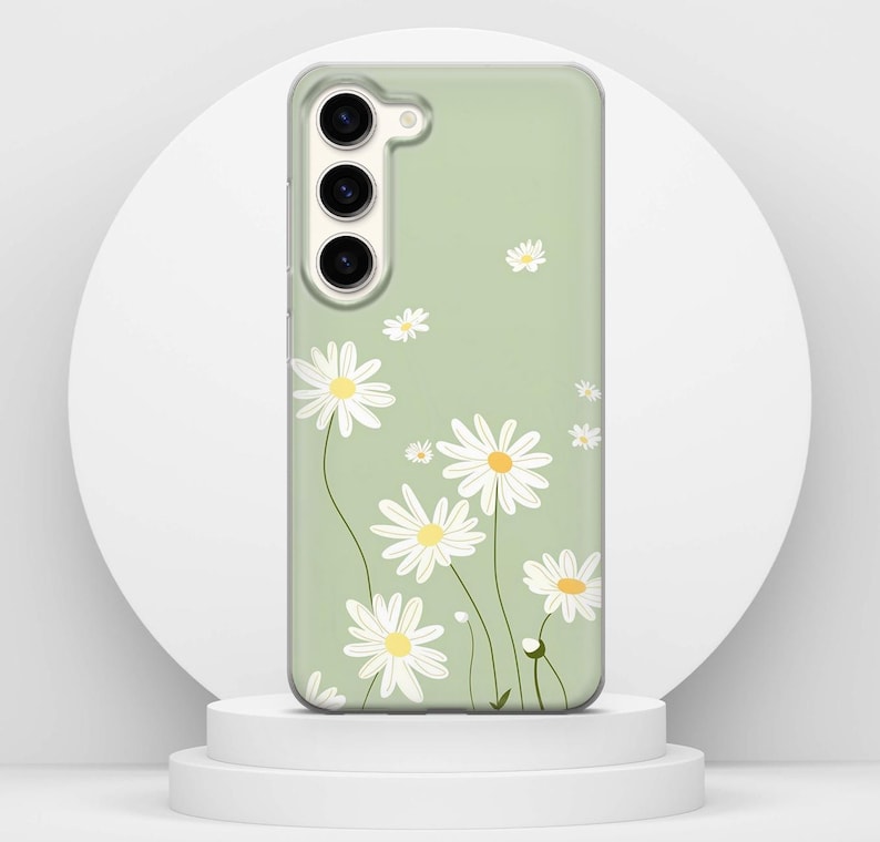 May include: A clear phone case with a pale green backdrop, decorated with a daisy floral pattern. The daisies have white petals and yellow centres. The case has camera and button cutouts.