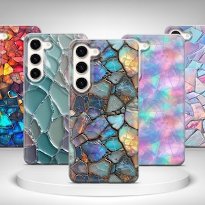 May include: A collection of five smartphone cases with a mosaic design. The cases feature a variety of colors, including red, orange, blue, green, and purple. The cases are displayed on a white, circular platform.