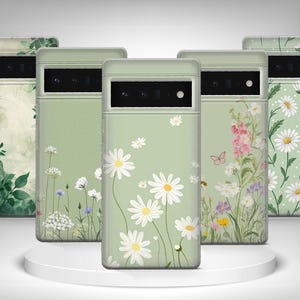 May include: Five phone cases with floral patterns. The cases have a pale green base with designs of daisies, wildflowers, and green leaves. The cases are displayed on a white, circular platform. The cases are for a mobile phone.