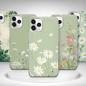 May include: A selection of phone cases with floral patterns. The cases showcase designs such as daisies, wildflowers, and botanical prints in green, white, and pink hues. The cases are presented on a white circular platform.