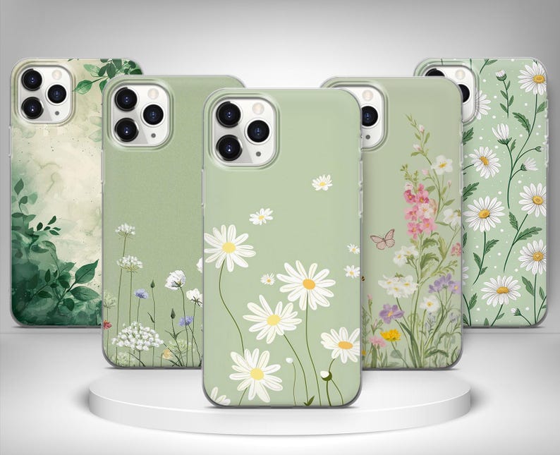 May include: A selection of phone cases with floral patterns. The cases showcase designs such as daisies, wildflowers, and botanical prints in green, white, and pink hues. The cases are presented on a white circular platform.