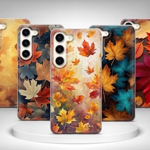 May include: Five phone cases with autumn leaf designs. The cases feature a variety of colors, including orange, yellow, red, and blue. The leaves are depicted in a watercolor style, with a blurred background. The cases are displayed on a white, circular platform.