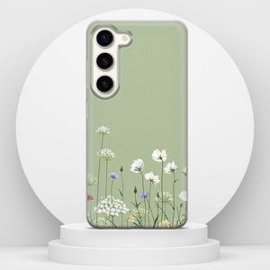 May include: A sage green phone case with a floral pattern. White, blue, and yellow wildflowers are shown at the base of the case. The phone case has a camera cutout and buttons.