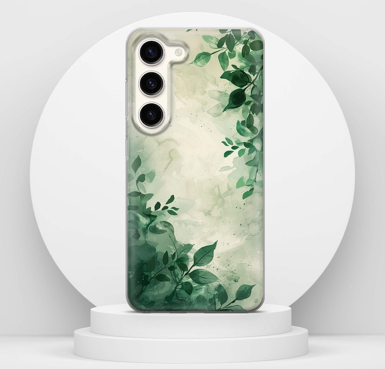 May include: A phone case with a watercolour design of green leaves and foliage. The case has a clear background with a soft, blurred effect. The leaves are in varying shades of green, creating a natural, botanical theme.