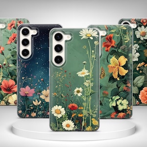 Può includere: Una collezione di custodie per telefoni con disegni floreali. Le custodie presentano vari fiori nei toni del rosso, arancione, giallo e bianco su uno sfondo verde e blu scuro. Le custodie sono esposte su una piattaforma circolare bianca.
