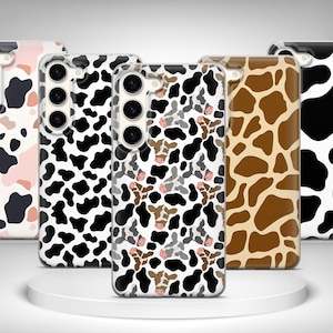Op de afbeelding: Een verzameling van vijf telefoonhoesjes met verschillende dierenprints. De hoesjes hebben patronen zoals koeienvlekken in zwart en wit, bruine giraffevlekken en een roze en zwarte koeienprint. De hoesjes worden getoond op een wit platform.