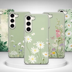 Puede incluir: Una colección de fundas para teléfonos con diseños florales. Las fundas presentan varios patrones, incluyendo margaritas, flores silvestres y detalles verdes. Las fundas son en tonos verdes y blancos.