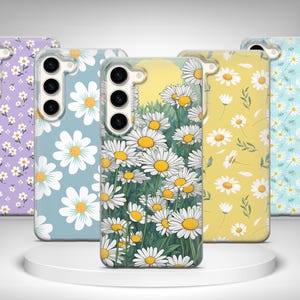 May include: Five phone cases with daisy floral patterns. The cases display a range of colours, including purple, blue, yellow, and green. The daisy designs vary, with some cases showing a field of daisies and others featuring scattered floral arrangements.