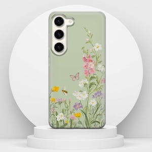 May include: A phone case featuring a floral design. The case has a pale green background with a colourful illustration of wildflowers, a butterfly, and a bee. The flowers are pink, yellow, white, and purple.
