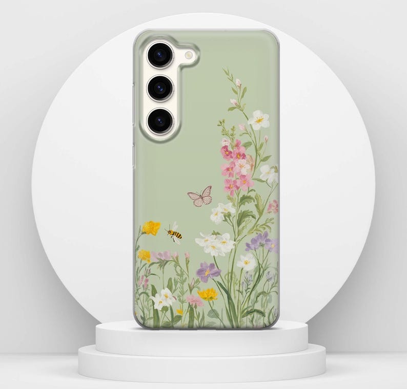 May include: A phone case featuring a floral design. The case has a pale green background with a colourful illustration of wildflowers, a butterfly, and a bee. The flowers are pink, yellow, white, and purple.