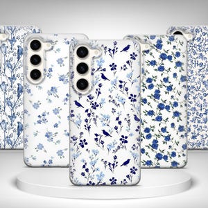 Op de afbeelding: Een verzameling van vijf telefoonhoesjes met bloemen- en vogelontwerpen. De hoesjes hebben een witte achtergrond met blauwe bloempatronen en vogel silhouetten. De hoesjes worden gepresenteerd op een wit, rond platform.