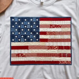 Könnte beinhalten: Weißes T-Shirt mit einem Patchwork-Design der amerikanischen Flagge. Die Flagge enthält Denim, rot-weiß gemusterte Stoffe und weiße Sterne auf blauem Denim-Hintergrund. Das Shirt trägt die Worte "DIGITALE DOWNLOADS" und Dateityp-Symbole.