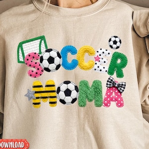Könnte beinhalten: Beiges Sweatshirt mit den Worten "Soccer Mom" in bunten, strukturierten Buchstaben. Das Design umfasst Fußbälle, ein Tor und eine Schleife. Die Wörter "Sofort-Download" und "Digitale Downloads" sind ebenfalls sichtbar.