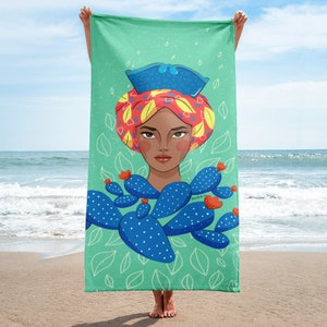 Può includere: Un asciugamano da spiaggia turchese con un'illustrazione colorata di una donna che indossa un turbante rosso, giallo e blu. Il viso della donna è visibile ed è circondata da piante di cactus blu e verdi.