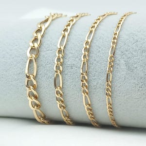 May include: Four gold chain necklaces of varying widths, displayed on a gray fabric background.