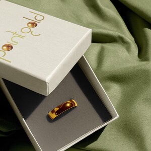 May include: A gold ring in a white box with the logo "Point Gold" on the lid. The box is on a green fabric surface.