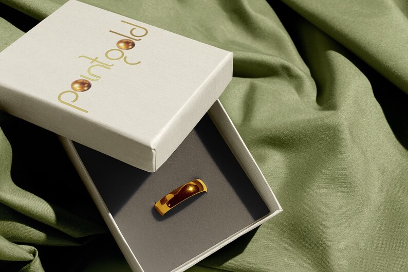 May include: A gold ring in a white box with the logo "Point Gold" on the lid. The box is on a green fabric surface.