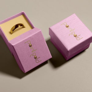 May include: Two pink boxes with the text "portgold" in gold lettering. One box is open and contains a gold ring.