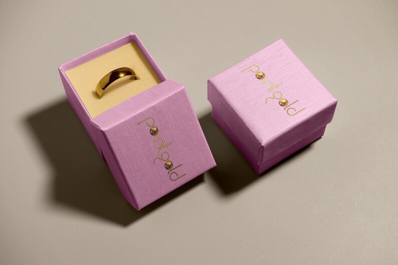 May include: Two pink boxes with the text "portgold" in gold lettering. One box is open and contains a gold ring.