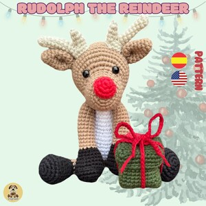 May include: Crocheted Rudolph the Reindeer amigurumi toy holding a green gift box with a red ribbon. The reindeer is brown with a red nose and black hooves. The toy is sitting in front of a green Christmas tree.